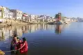 Drei Personen in farbenfrohen Saris bei einer rituellen Waschung im heiligen Pushkar-See, einem Highlight der Rajasthan-Reise, mit den Ghats und der Stadt Pushkar im Hintergrund.