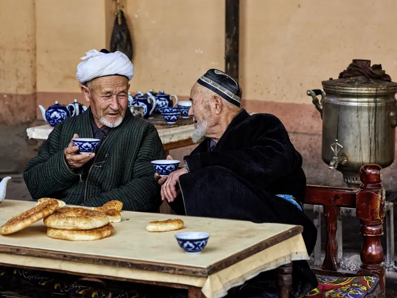 Auf unserer Rundreise durch Usbekistan und Kirgisistan sehen wir einheimische alte Männer beim Teetrinken ins Gespräch vertieft. Die blauen Teeschälchen mit Baumwollmuster sind typisch für Usbekistan, die kreisrunden Fladenbrote ebenso.