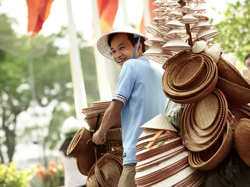 Ein vietnamesischer Verkäufer fährt mit dem Fahrrad durch die trubeligen Straßen Hanois und bietet typische vietnamesische Reishüte zum Verkauf an.