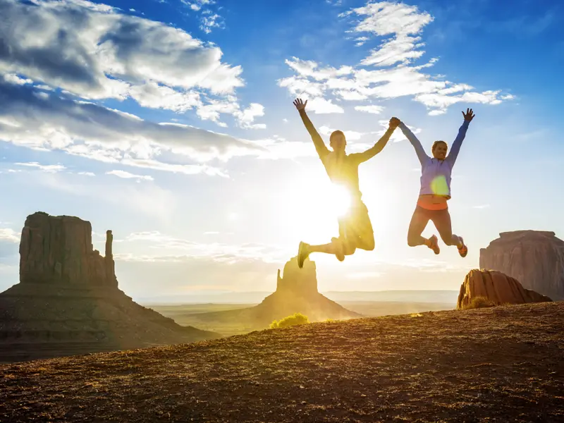 Junge Traveller springen freudig in die Luft vor dem Hintergrund des Monument Valley, ein Highlight dieser Rundreise durch den Westen der USA.