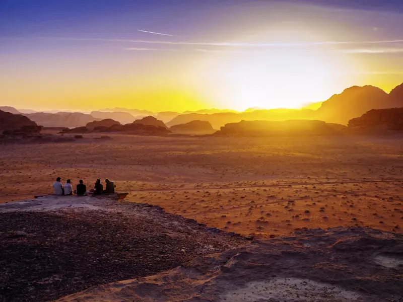 Auf der Marco Polo Rundreise durch Jordanien genießt die Gruppe den Sonnenuntergang in der  Wüstenlandschaft Wadi Ram.