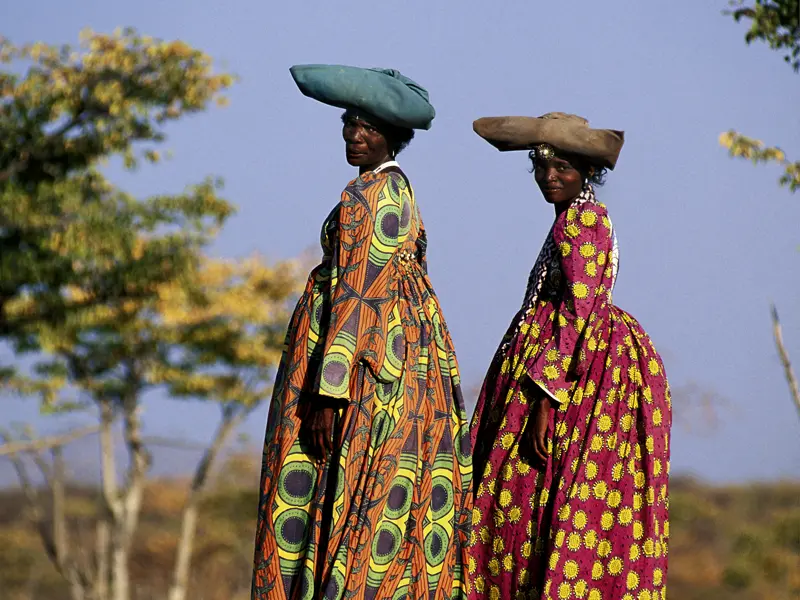 Entdeken Sie Namibia mit Marco Polo Reisen! Sie spüren den Atem der Wildnis, doch neben der grandiosen Tierwelt begegnen Sie auch der einheimischen Bevölkerung. Hier zwei Frauen in traditionellen viktorianischen Kleidern mit Hut.